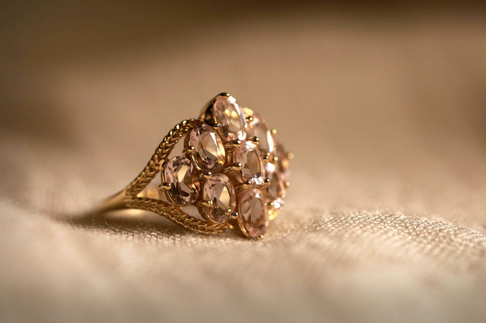 Macro shot of a gold cluster ring set with pink gemstones resting on warm textured fabric