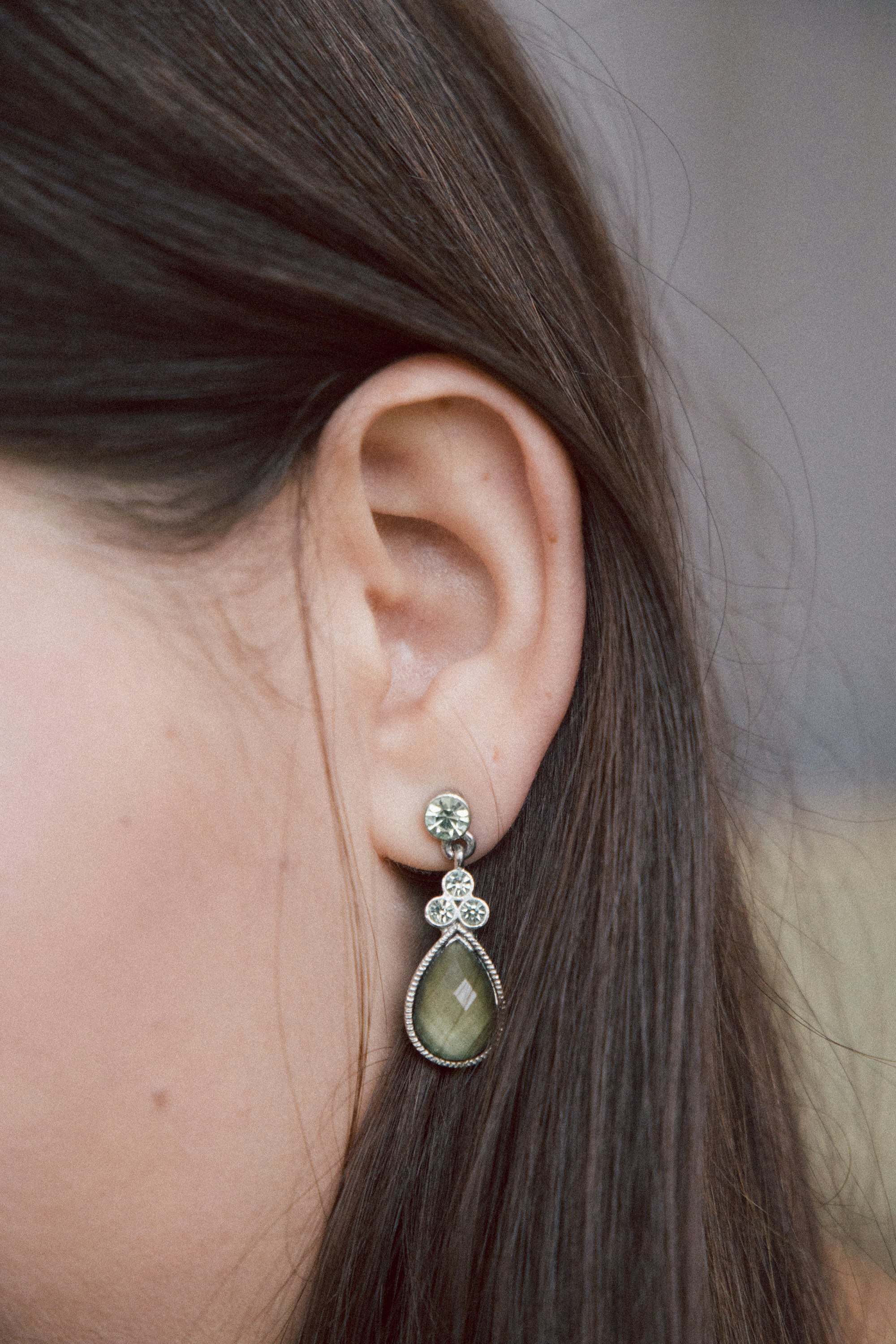 Close-up of an ear wearing a delicate gemstone drop earring, hair falling softly around it