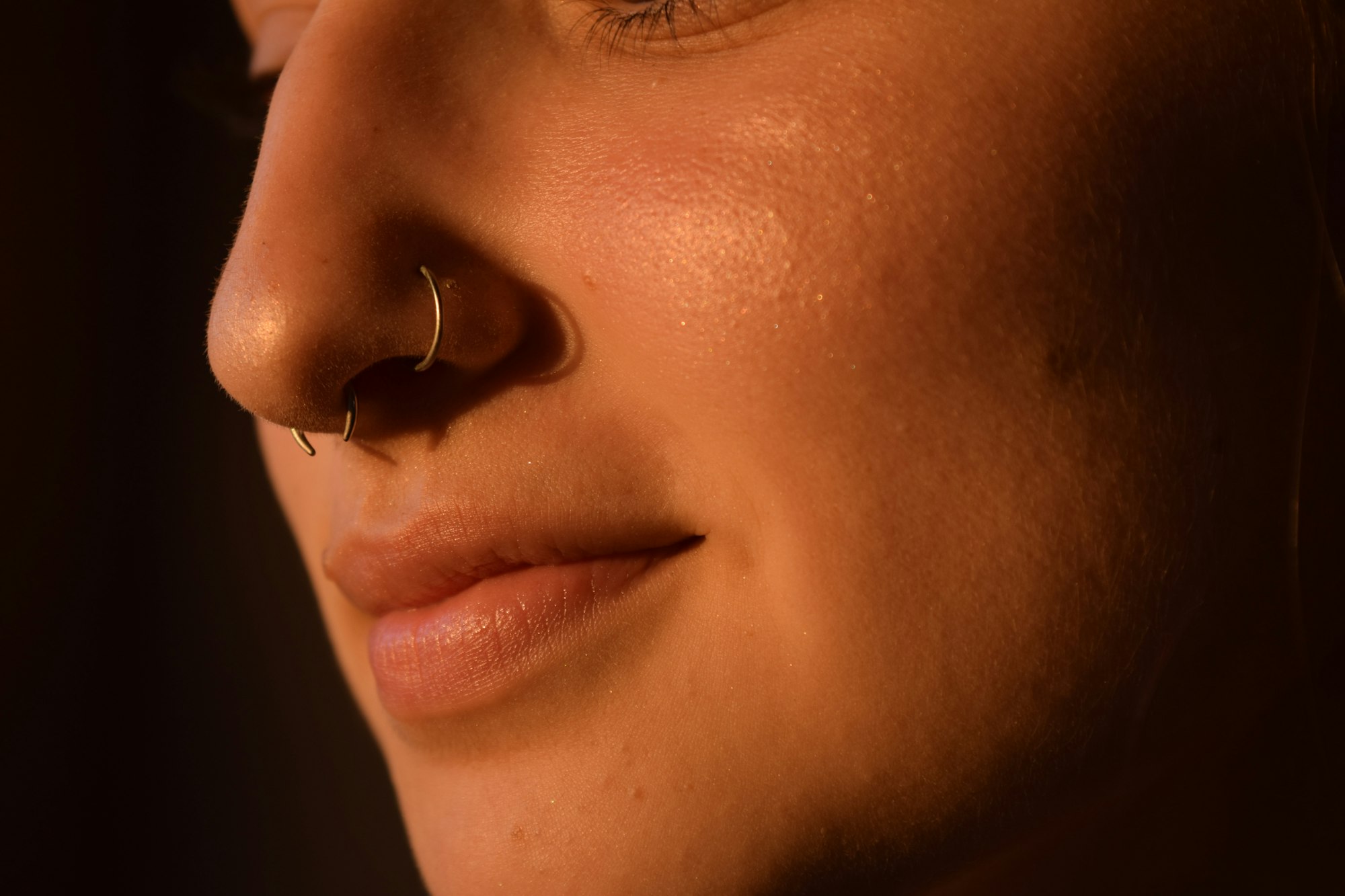 Moody black-and-white portrait showing eyebrow, septum, lip, and ear piercings