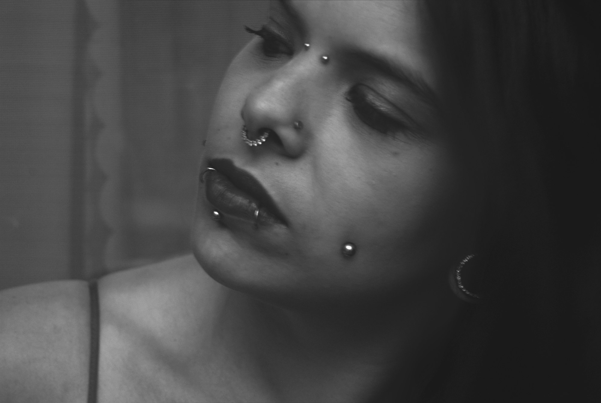 Black-and-white close-up of a septum ring and eyebrow piercing against a soft background