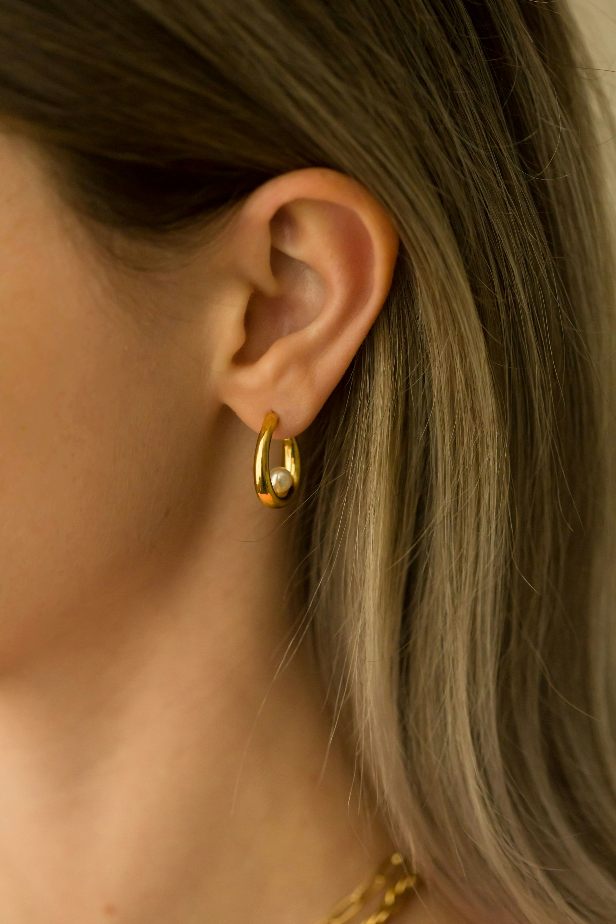 Close-up of an ear wearing a polished gold hoop earring with a pearl detail