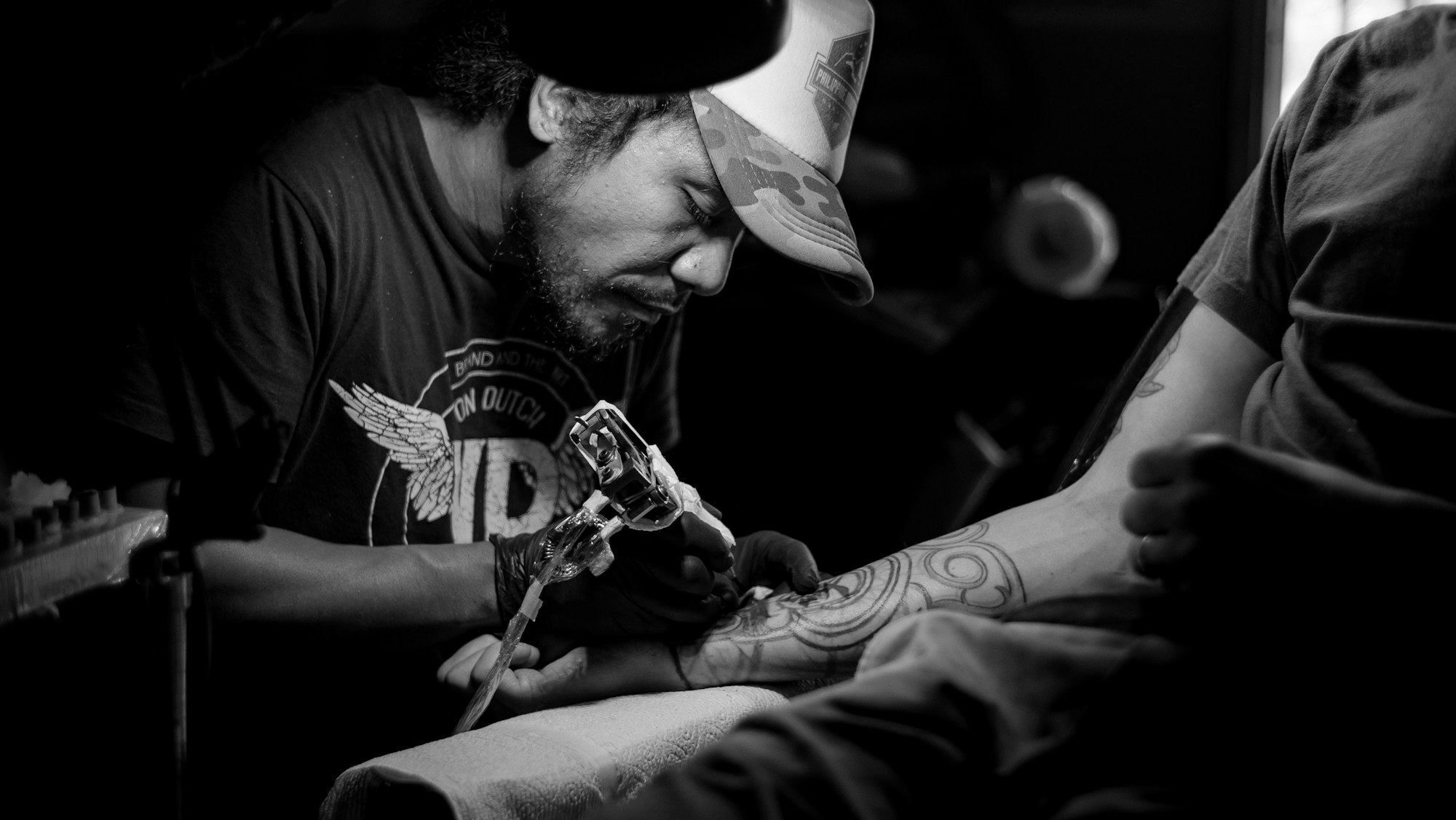 Grayscale close-up of a tattoo artist tattooing intricate linework onto skin