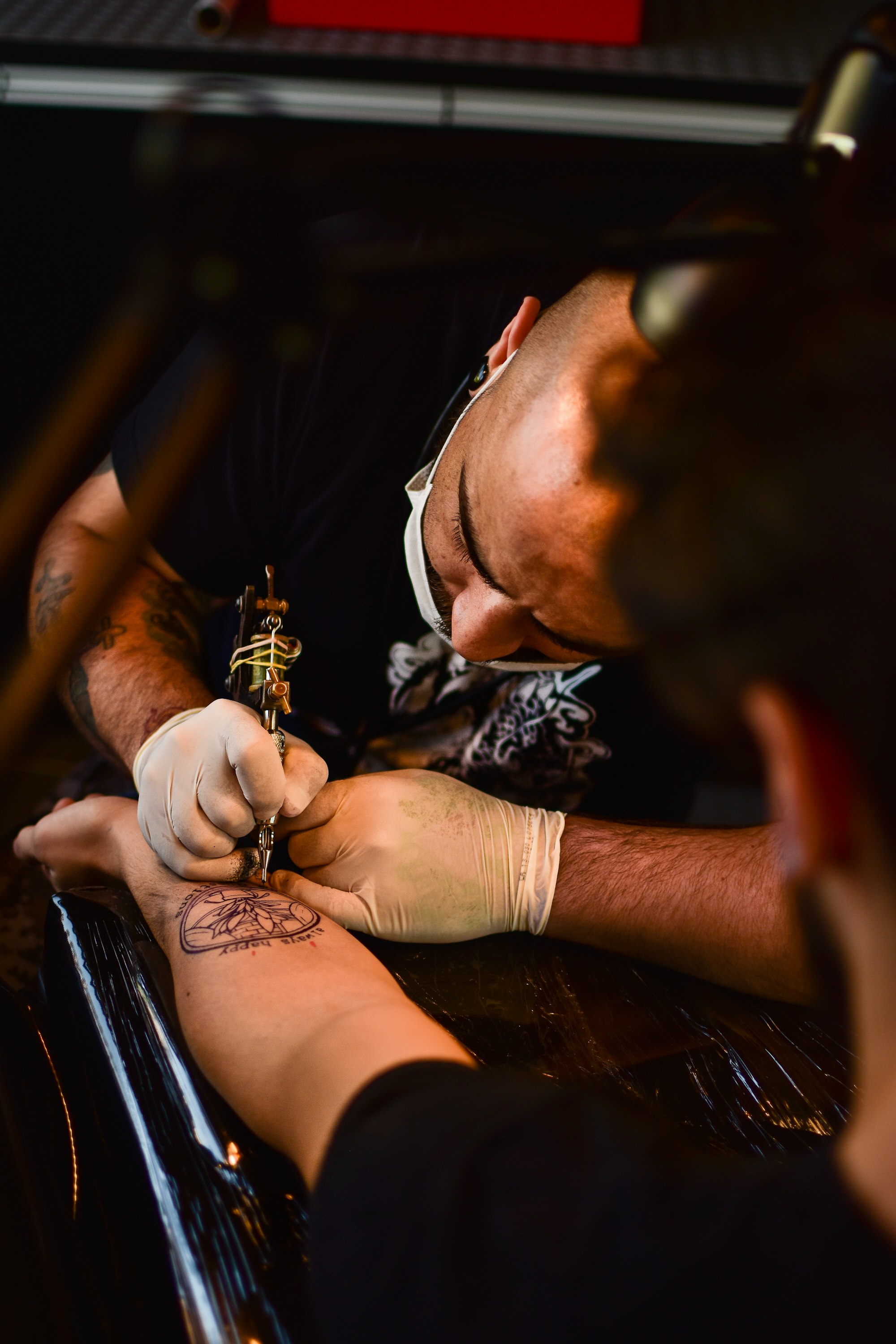 Black-and-white photo of a tattoo artist at work, tattoo machine and towel-draped station in view