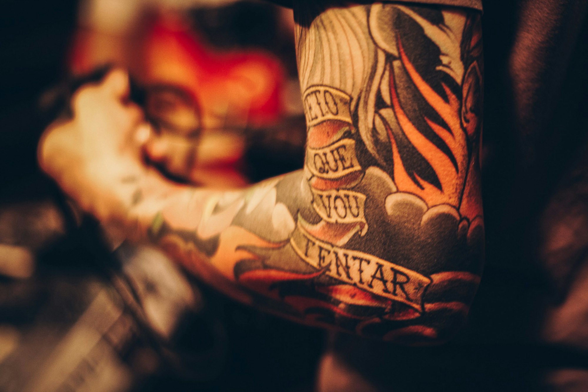 Tattoo artist masked and focused, tattooing a small piece on a client’s forearm
