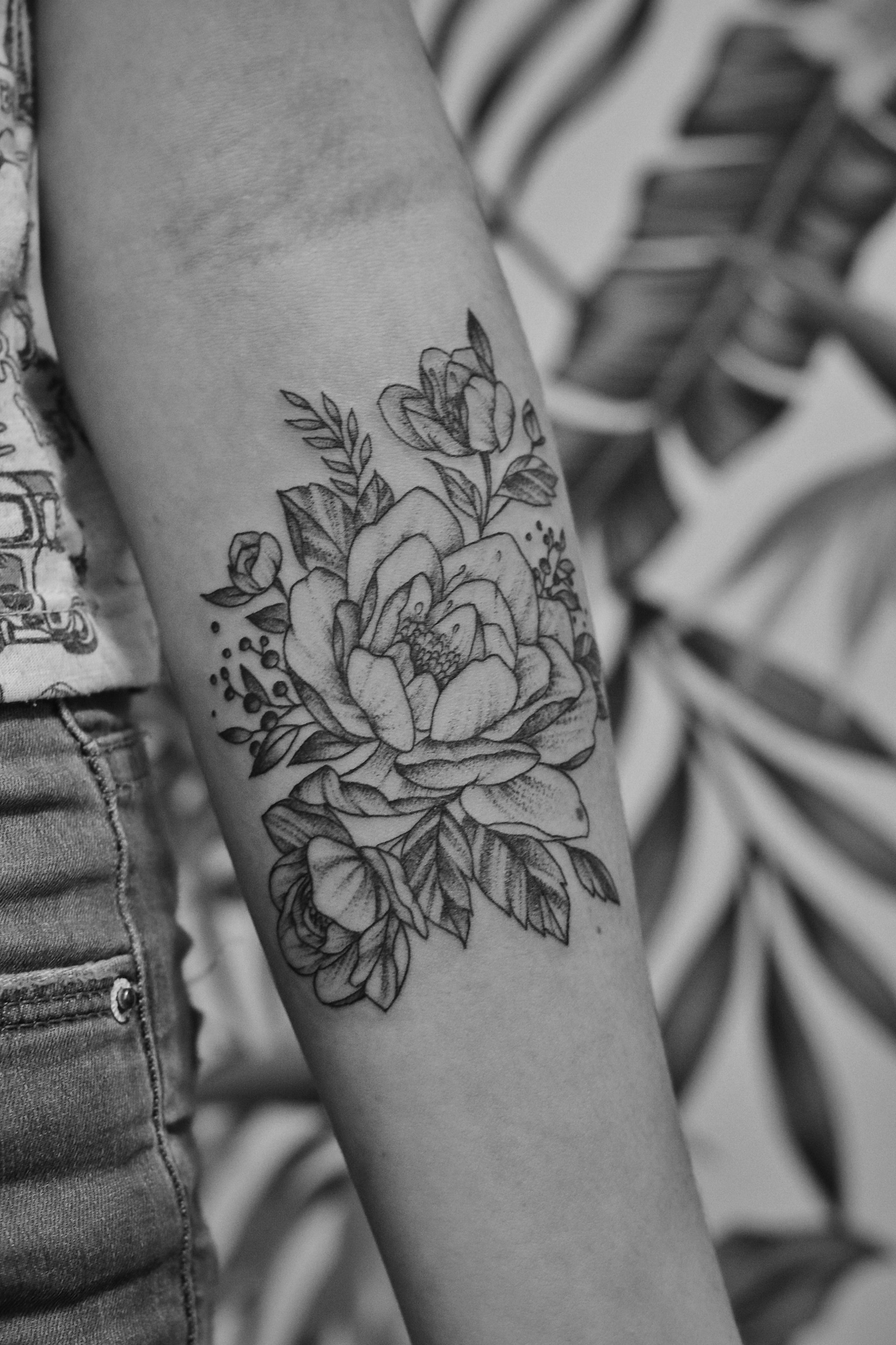Close-up color photo of a finished fine-line floral tattoo on a forearm, warm lighting